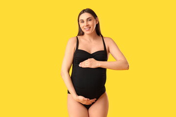 Young pregnant woman in swimsuit on yellow background. Travel concept