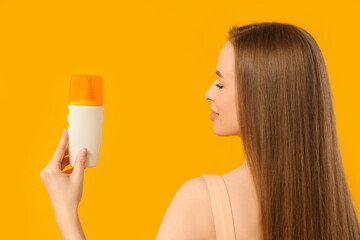 Beautiful young woman with bottle of sunscreen cream on yellow background
