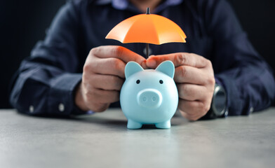 Businessman covering piggy bank by orange umbrella. Concept for finance insurance, protection and safe investment or banking