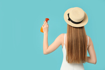 Beautiful young woman with bottle of sunscreen cream on blue background, back view
