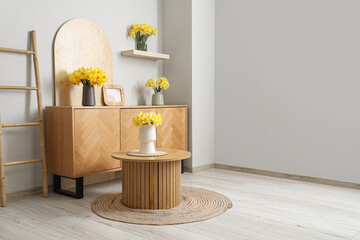 Vases with yellow narcissus flowers on coffee table and chest of drawers in white room