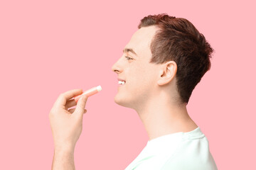 Handsome young man with lip balm on pink background