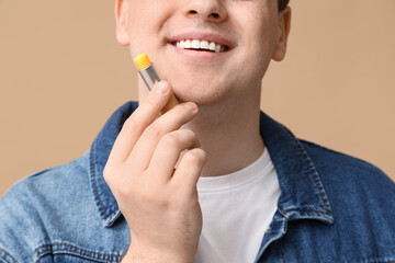 Young man with lip balm on brown background, closeup