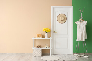 Stylish interior of modern hall with hanger, daffodil flowers on shelving unit and door