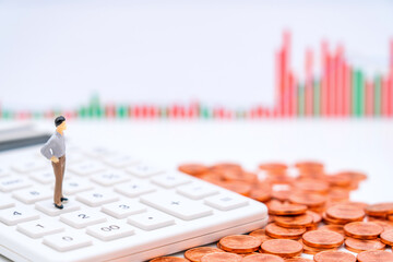 Toy figurines and many coins on a calculator under the background of a candlestick chart - the concept of stock finance