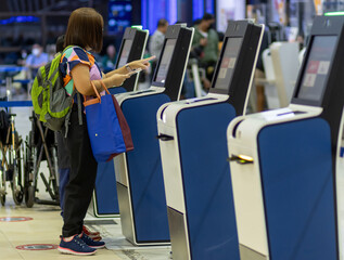 A woman using self check-in kiosks in airport terminal.