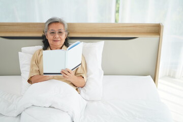 Happily elderly woman lying on bed and reading book