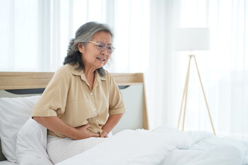 Mature Woman sitting on bed and holding her stomach with feels stomachache