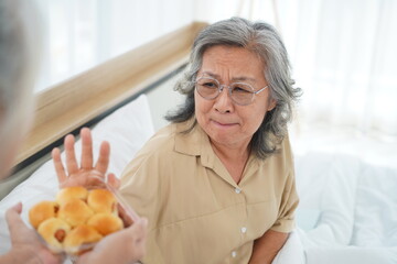 Asian senior woman raised her hand to refuse bread from caregiver
