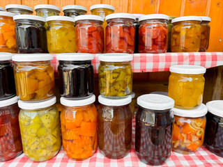 Assortment of homemade preserves in glass jars with checkered cloth, various pickled fruits and vegetables, colorful display, canned goods collection, close up with selective focus.