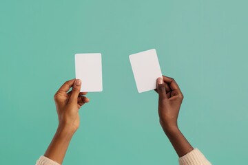 Two hands holding blank white cards on a teal background.
