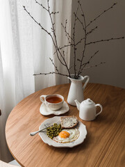 Cozy breakfast, brunch - tea, fried egg with canned peas and bread and butter on a round wooden table - 789882339