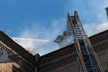 Fototapeta premium Rescuers are putting out the fire. A damaged residential building after a massive rocket attack. Heavy smoke. The house is on fire.