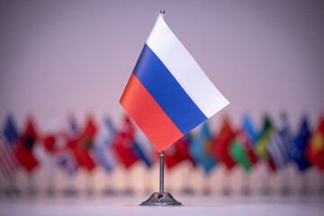 A small Russian flag flies among a row of other flags under an electric blue sky