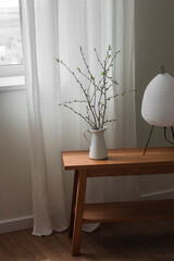 A cozy corner of the living room - a jug with branches, a paper lamp on a wooden bench next to the window