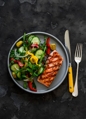 Delicious diet lunch, dinner - grilled salmon and fresh vegetable salad on a dark background, top view