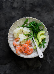 Lunch diet - rice, shrimp, boiled cauliflower, arugula, avocado in one plate on a dark background, top view - 789887990