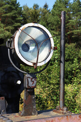 An abandoned spotlight from a retro steam locomotive against the backdrop of a forest.