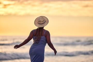 Back, sunset or black woman at beach walking to relax on holiday vacation for outdoor break in Greece. Tourist, girl or African person looking at ocean, nature or sea with peace, wellness or travel