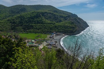 Black Sea, beach and steep shore near the green wooded mountains of the Western Caucasus near the village of Durso (South of Russia) on a sunny spring day