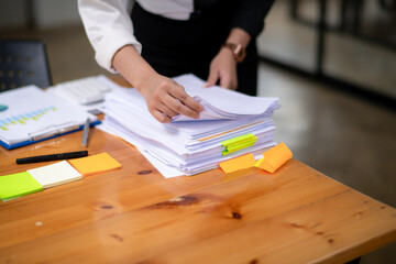 Focused businesswoman in a two-tone shirt sorting through stacks of paperwork at a wooden desk in...