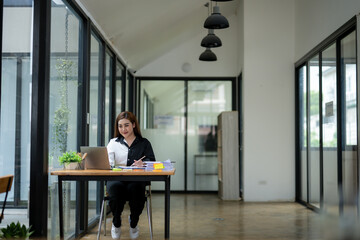 Portrait of a poised Asian businesswoman in a white suit standing confidently in a contemporary office workspace.