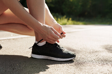 Close-up of a runner's hands tying shoelaces on athletic shoes on a sunny path, ready for jogging.