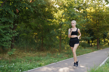 A fit young woman with a pixie haircut is shown jogging on a scenic park path surrounded by lush...