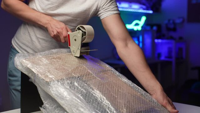Male hands holding packing duct tape gun roller dispenser and sealing monitor with sticky adhesive tape. Packing up furniture and home belongings in packages with adhesive roller for relocation.