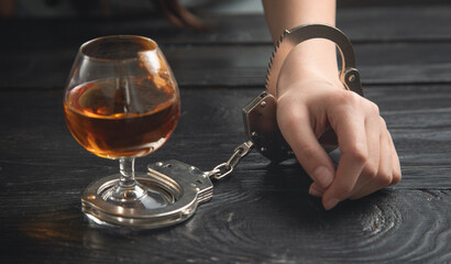 Human hand in handcuffs with a glass of cognac.