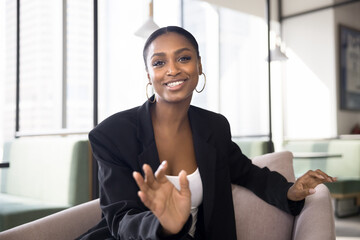 Cheerful young African business consultant woman in formal suit talking on video conference call, speaking at camera, moving hand, giving online consultation. Screen portrait in co-working space