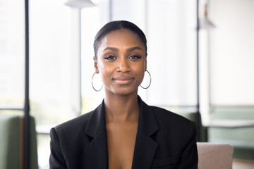 Positive beautiful African American businesswoman in formal jacket head shot portrait. Female business leader, entrepreneur, professional, manager standing for in co-working space, looking at camera