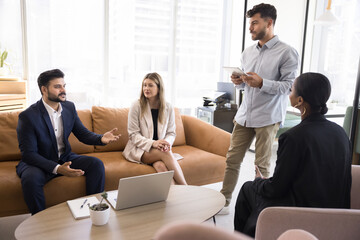 Serious motivated Indian professional man offering creative ideas to diverse team on meeting, speaking to multiethnic colleagues. Business coworkers brainstorming on couch in office lobby