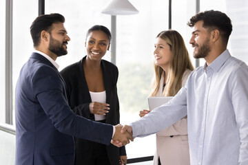 Happy confident diverse male business partners shaking hands at meeting, standing in office hall, closing deal, getting agreement, finishing successful work project with handshake