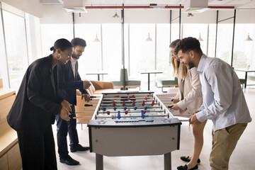 Group of happy engaged multiethnic colleagues playing toy football, fighting in table soccer, having fun, enjoying office leisure environment, work break activity, laughing at board game