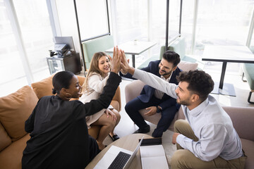 Cheerful diverse business colleagues celebrating successful startup. Office friends clapping hands in high five gesture, achieving success together, enjoying partnership, teamwork