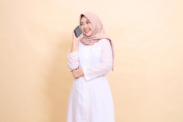 woman indonesia muslim wearing a hijab candidly smiling and laughing while holding a cell phone gadget in her hand while calling someone. Lifestyle, technology and promotion concept