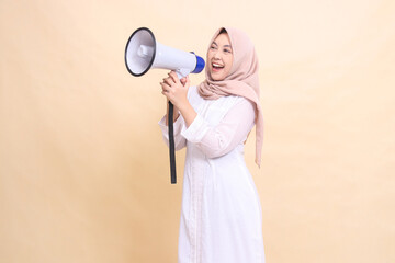 woman asian young wearing hijab slanted to the right candidly shouts cheerfully holding a loudspeaker megaphone with both hands. Technology, broadcast and promotion concept