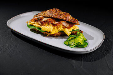 Delicious croissant sandwich with scrambled eggs, bacon, and avocado on a plate