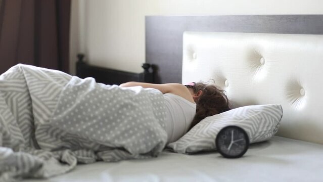 Cute little kid girl sitting on bed waking up in morning shocked looking alarm clock.