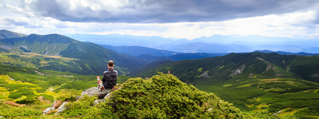 Man and dog thoughtfully enjoying the mountain landscape view of the valley. Beautiful green landscape. Friendship and loneliness concept. Long horizontal banner wild nature