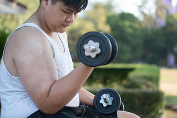 Asian chubby teenboy doing exercise with dumbbells lifting in outdoor park in late afternoon of the day.
