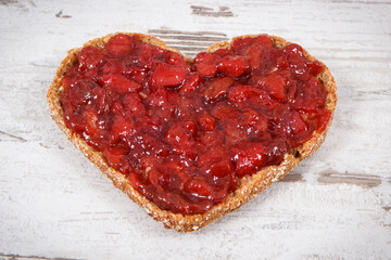 Slice of bread with strawberry jam for breakfast. Shape of heart. Rustic background
