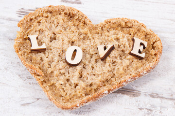 Wholegrain bread in shape of heart for breakfast and inscription love. Old rustic background