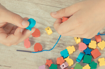 Preschooler making bracelet from thread and wooden colored beads. Development of kids motor skills,...
