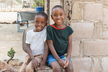 village two african children ,sited on a chair in the yard, casual dressed