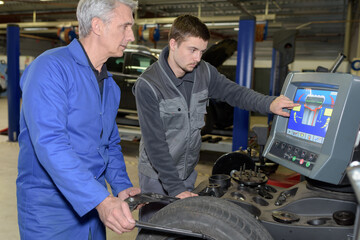 apprentice mechanic and teacher retreading wheel in automotive workshop