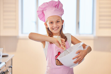 Girl, portrait and baking in kitchen with chef hat for learning, child development and fun in...