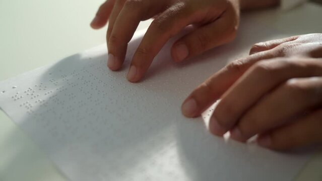 Hand of a blind person reading some braille text on page paper to learn. Finger of blind student touching the braille alphabet Code on sheet. Disabled person concept.