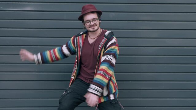 Funny dancer in hat, glasses and hip sweater having fun outdoors. Guy dancing modern electro swing dance.